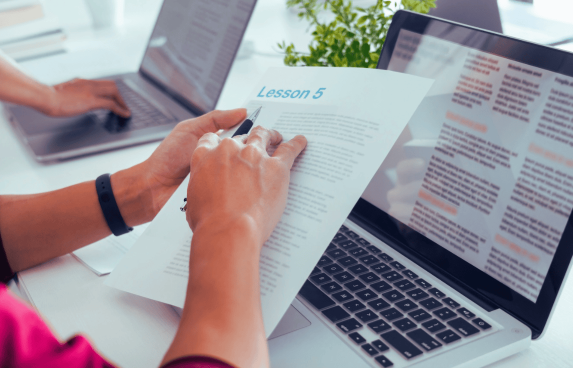 Business professional sitting at desk and studying English on computer and with printed notes